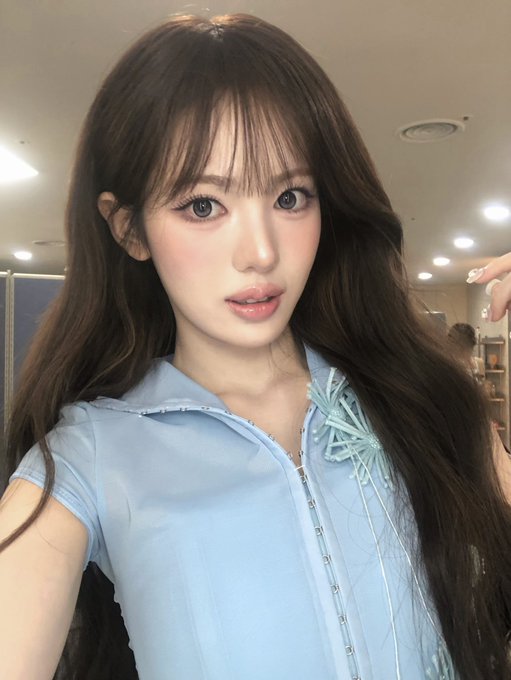 A selfie of a young woman with long dark hair wearing a light blue collared top with a bow.