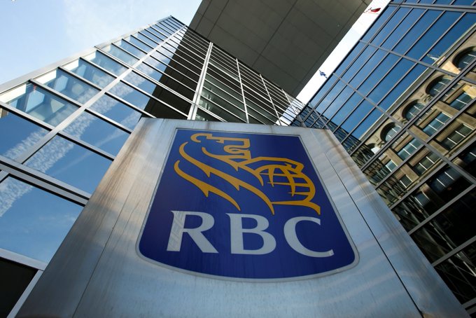 A low-angle shot captures the RBC (Royal Bank of Canada) logo sign in front of modern glass skyscrapers under a partly cloudy sky.