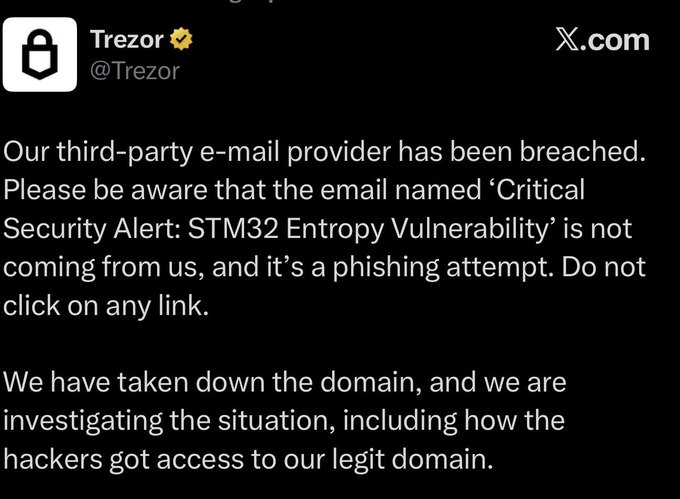 A screenshot of a post from Trezor's verified X (formerly Twitter) account (@Trezor) warning users that a phishing email titled "Critical Security Alert: STM32 Entropy Vulnerability" was sent from their legitimate domain after a third-party email provider breach, advising recipients not to click any links while the company investigates.