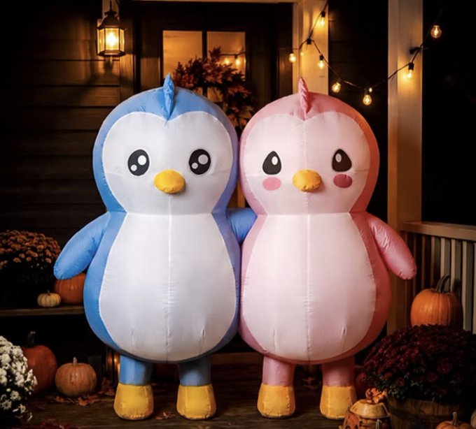 Two large inflatable penguin decorations, one blue and one pink, displayed outdoors with pumpkins and string lights in a Halloween/fall setting.