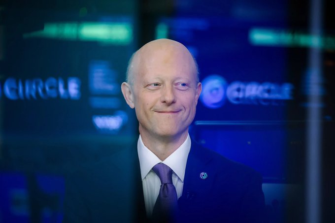 Circle CEO Jeremy Allaire smiles in front of a backdrop displaying the Circle logo, seemingly marking the irony of his past Bitcoin dismissal now that Circle has launched a wrapped-BTC lending product.