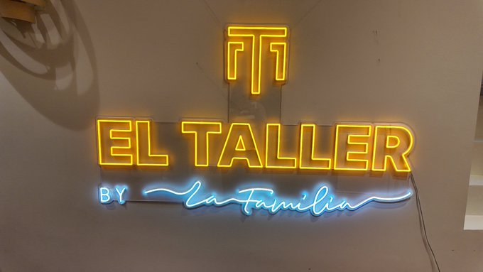 A neon sign reading 'EL TALLER BY La Familia' in yellow and blue lights.