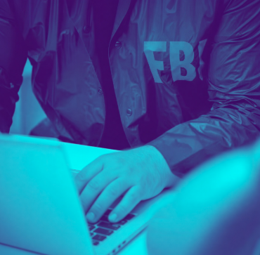 A person wearing an "FBI" jacket types on a laptop, with the image color-tinted in blue, illustrating the federal investigation and prosecution of a Colombia-based crypto broker sentenced to 160 months for laundering drug trafficking proceeds through USDT and participating in a cocaine importation scheme.