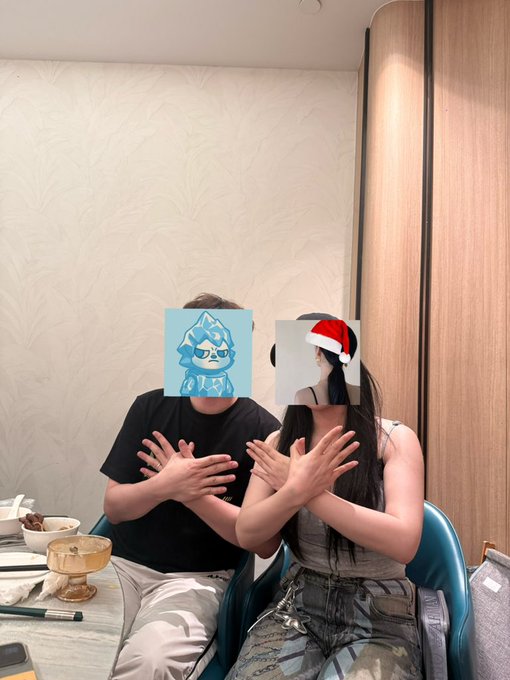 Two people sit at a dining table with their faces obscured by memes (a blue anime character and a penguin wearing a Santa hat), both holding their hands up in an 'X' gesture.