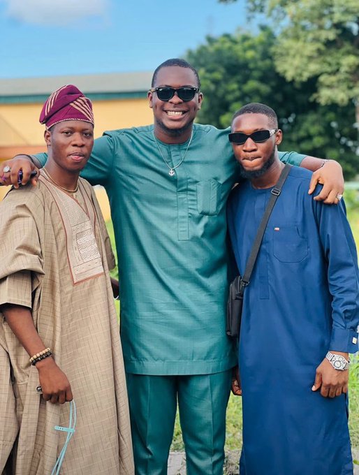 Three men pose together outdoors, with the central figure wearing a teal traditional outfit and sunglasses, flanked by a man in a beige agbada with a maroon cap on the left and another in a navy blue kaftan with a crossbody bag on the right, capturing a moment of camaraderie between the friends and mentors referenced in the post.