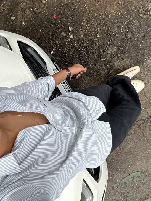 A person wearing an unbuttoned blue striped shirt and black pants, holding car keys while standing next to a white car.