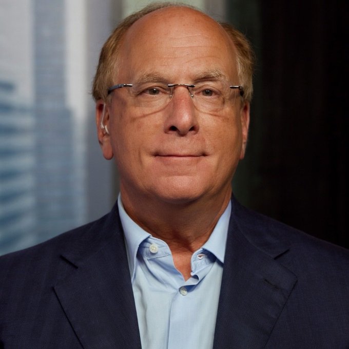 A headshot of an older, balding man wearing glasses, a light blue button-down shirt, and a dark blue blazer.