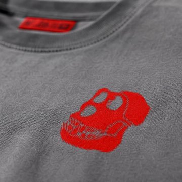 A close-up shot of a gray t-shirt featuring a red embroidered Bored Ape Yacht Club (BAYC) skull logo on the chest, with a matching red neck tag visible at the collar, promoting ApeFest Early Access merchandise available at store.bayc.com before the September 4 deadline.