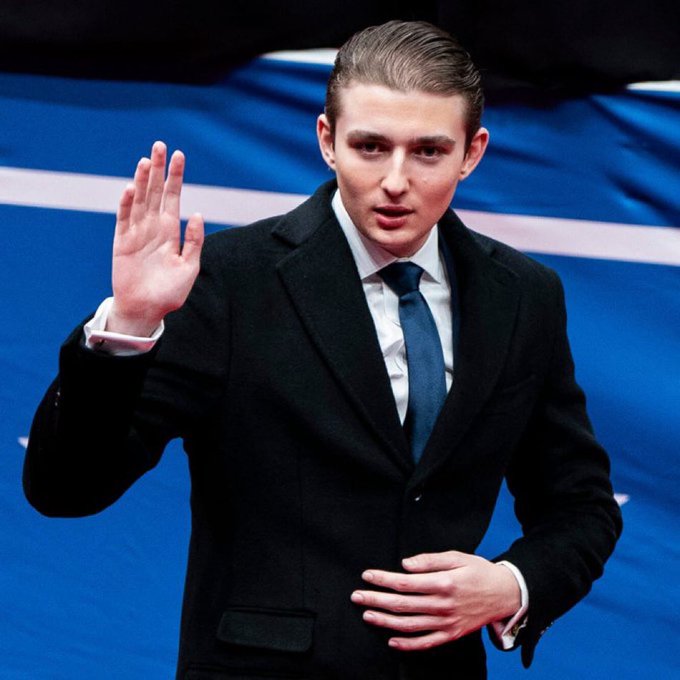 A young man in a black blazer, white shirt, and dark tie stands on a blue stage, raising his right hand with his palm facing forward in a gesture that appears to be addressing or signaling to an audience.

The image does not appear to relate to the accompanying post about the Quantum Financial System (QFS); rather, it shows what looks like a public speaker or performer in a formal setting, with no visible text, numbers, or tickers connecting it to cryptocurrency or digital asset topics.