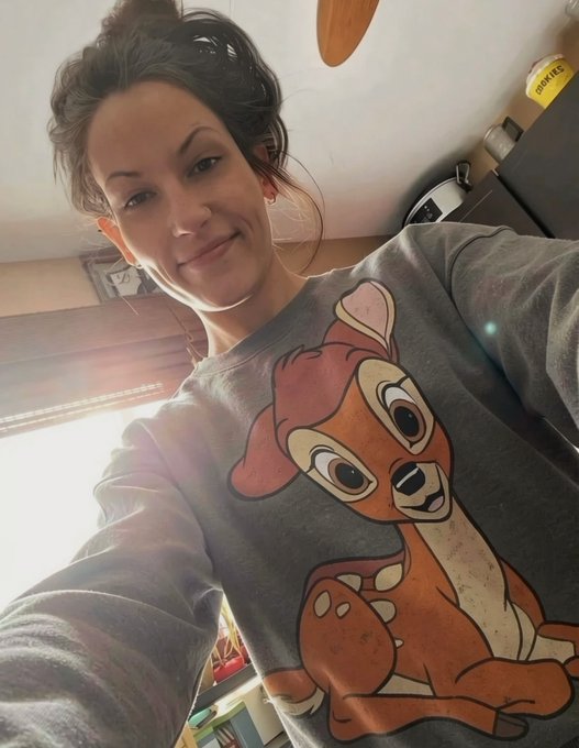 A selfie of a woman smiling, wearing a gray sweatshirt featuring a large graphic of Bambi the deer.