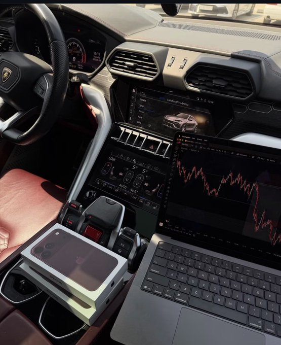 The interior of a Lamborghini Urus shows the dashboard and center console, with an iPhone box sitting in the cup holder area and a laptop displaying a downward-trending stock chart.