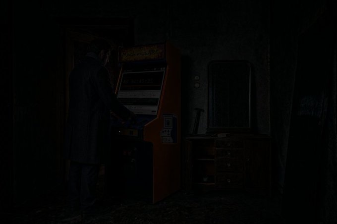Dark, dimly lit video game scene featuring a man in a long coat standing in front of an illuminated vintage arcade cabinet next to a wooden cabinet.