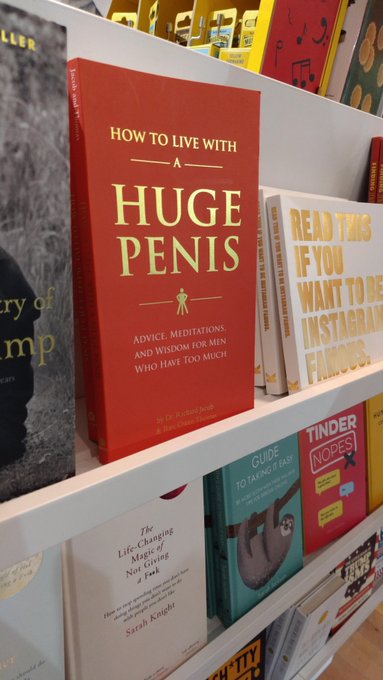 A bookstore display featuring the book 'How to Live with a Huge Penis: Advice, Meditations, and Wisdom for Men Who Have Too Much' by Dr. Richard Jacob and Brian E. Drake, alongside titles like 'Tinder Nopes' and 'The Life-Changing Magic of Not Giving a F*ck'.