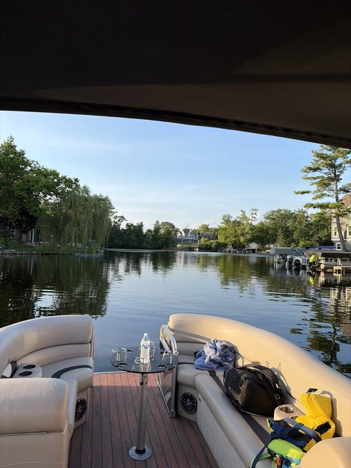 A view from a pontoon boat on a calm lake with trees and houses along the shore.