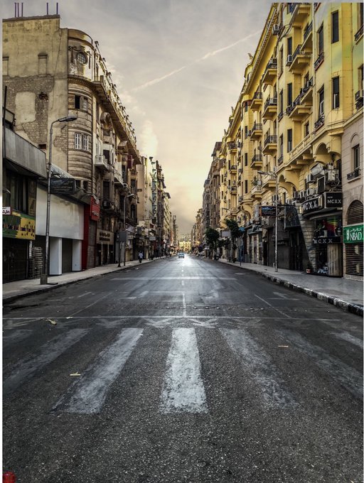 Empty street view of a European city at dawn or dusk, featuring classical architecture with balconies lining both sides of the road.