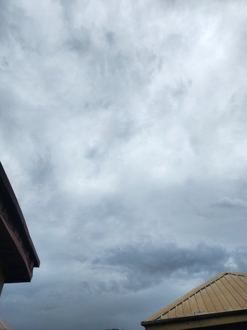 Overcast, cloudy sky viewed between the dark eaves of a roof on the left and a yellow metal roof on the right.