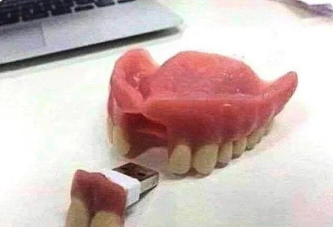 A set of pink dentures resting on a desk next to a USB drive that has been modified to look like small teeth.