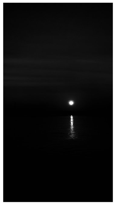 A bright moon or distant light shines over dark water at night, casting a narrow vertical reflection.