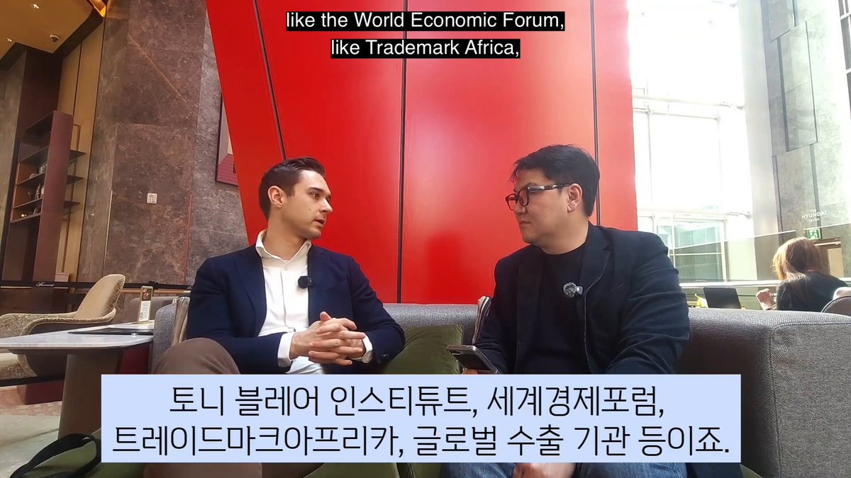 An interview setting shows two men seated on a couch in what appears to be a hotel lobby, with on-screen text referencing "the World Economic Forum" and "Trademark Africa," while Korean subtitles mention Tony Blair Institute, World Economic Forum, Trademark Africa, and global export standards. The image illustrates the discussion from Dom Schiener of TokenPost about the importance of government-recognized entities over offshore structures like BVI companies or Cayman Foundations.
