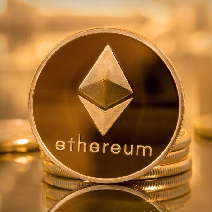 A close-up of a gold Ethereum (ETH) physical coin resting on a stack of gold coins, with the Ethereum logo and name clearly visible.