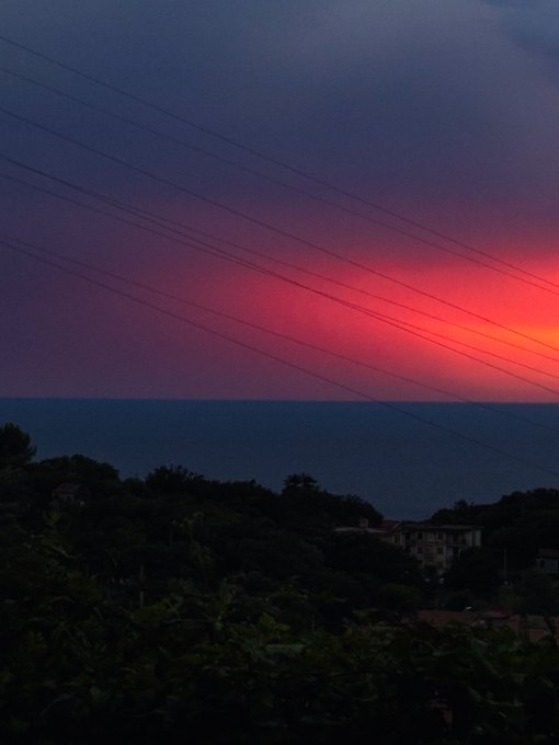 A twilight seascape with a gradient sky of deep purple and pink over a dark, silhouetted coastline crossed by power lines.