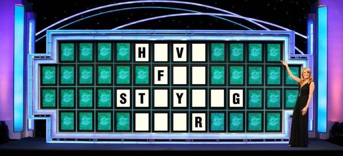 A Wheel of Fortune game show board with a woman in a black dress standing next to it, showing the letters H, V, F, S, T, I, Y, U, G, and R revealed.