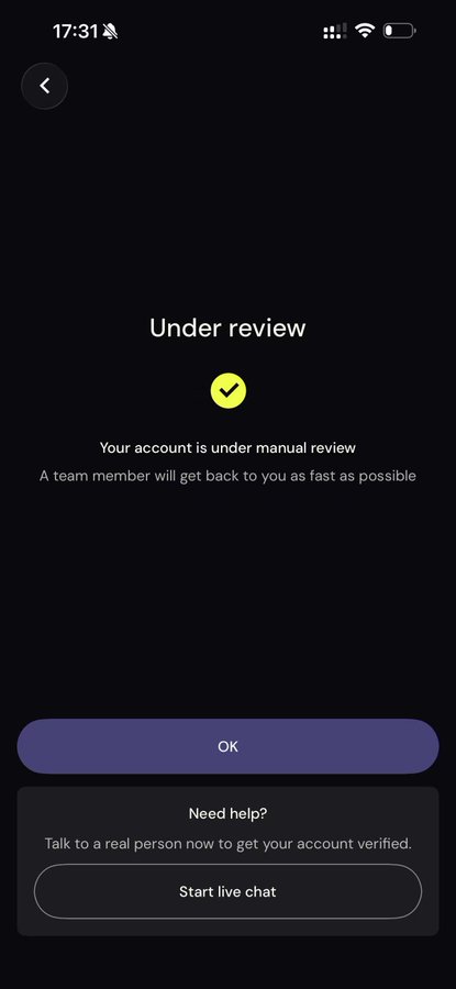 A smartphone screenshot displaying an 'Under review' screen with a yellow checkmark icon, stating 'Your account is under manual review' and offering buttons for 'OK' and 'Start live chat', with the time 17:31 visible at the top.