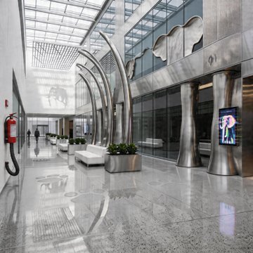 A modern building lobby featuring polished marble floors, curved metallic architectural columns, and large glass windows allowing natural light into the spacious corridor.
