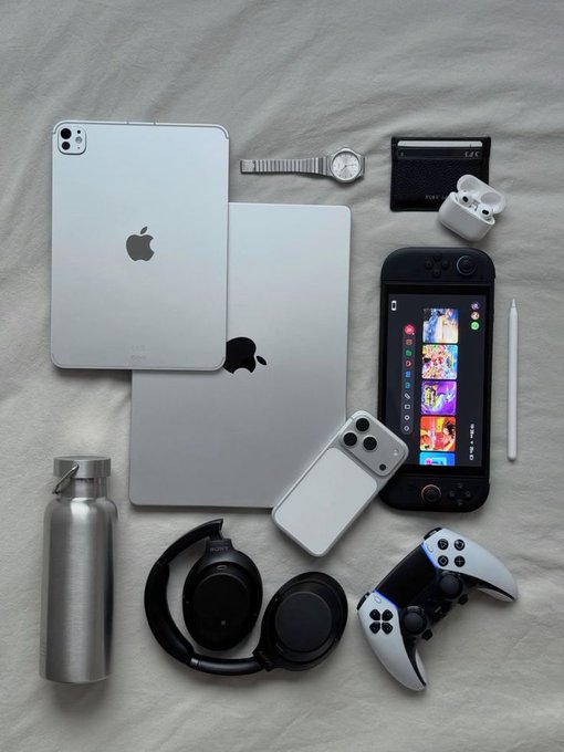 The image features a collection of electronic devices, including two Apple products (a tablet and a phone), headphones, a water bottle, and a wallet. The items are arranged on a bedspread or white sheet, creating an interesting mix of technology and everyday objects. The post seems to be discussing the importance of ecosystems in the gaming industry, with the focus on how companies like @NomismaNetwork and @RiverdotInc can grow through hype and strong infrastructure.