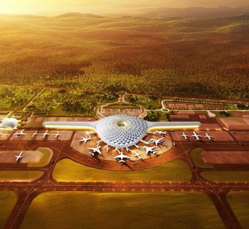 An aerial view of a futuristic circular airport terminal with aircraft parked around it, surrounded by green fields and distant mountains under a golden sunset.