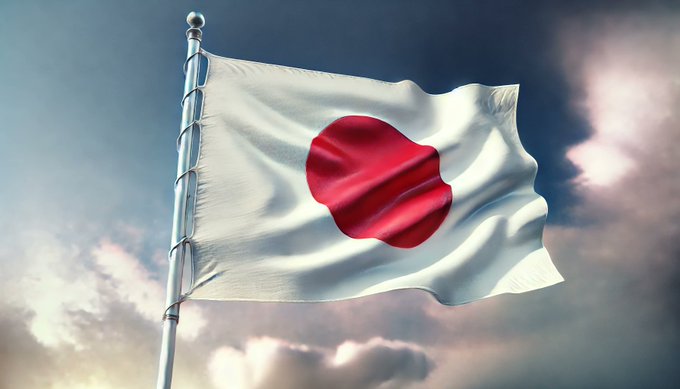 The flag of Japan, with a white background and red circle in the center, waving on a silver flagpole against a cloudy sky.