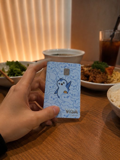 The image features a hand holding up a Visa credit card that has a penguin design on it. The text in the image suggests that someone who has already used this card might have done so for various purposes, such as buying coffee or paying for dinner. This implies that the person may be familiar with using KAST cards and possibly engaging in activities like online shopping or dining out.