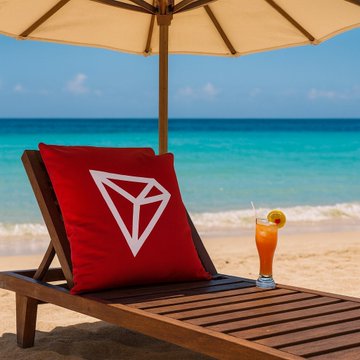 A red cushion displaying the TRON (TRX) logo resting on a wooden beach lounge chair next to a tropical cocktail with the ocean in the background.