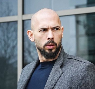 A bald, bearded man in a gray coat over a navy shirt stands outdoors looking serious, accompanying a post about Andrew Tate endorsing Bitcoin as a solution to the collapsed "Ponzi" economy and highlighting SpaceX's 18,712 BTC holdings worth $1.2 billion.