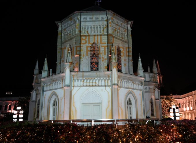 An illuminated white Gothic-style church at night is projected with the text "BUILD THE FUTURE" in gold, symbolizing the historic structure as a foundation for building the future with BNB Chain.