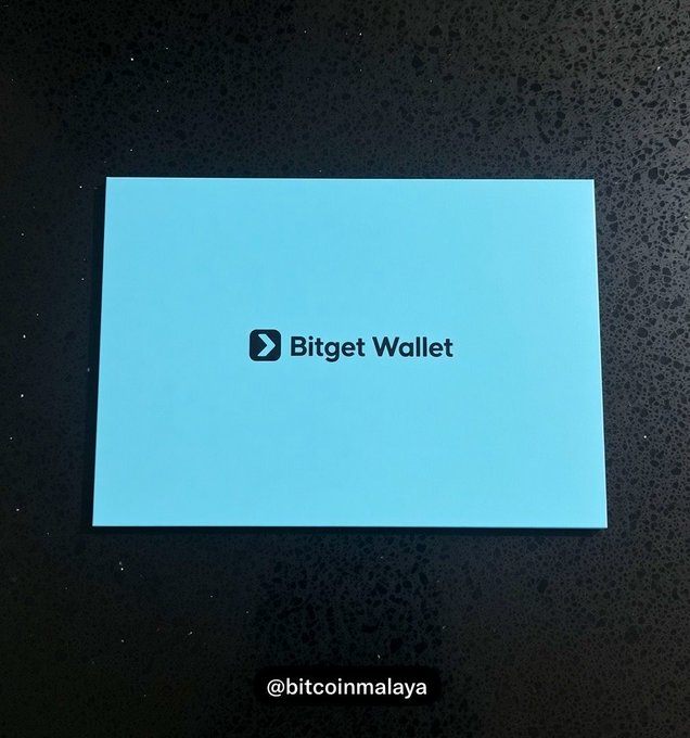 A teal "Bitget Wallet" envelope rests on a dark textured surface, with the caption "WHO NEEDS ONE" playfully suggesting the need for a crypto wallet, tying into the branded packaging shown.