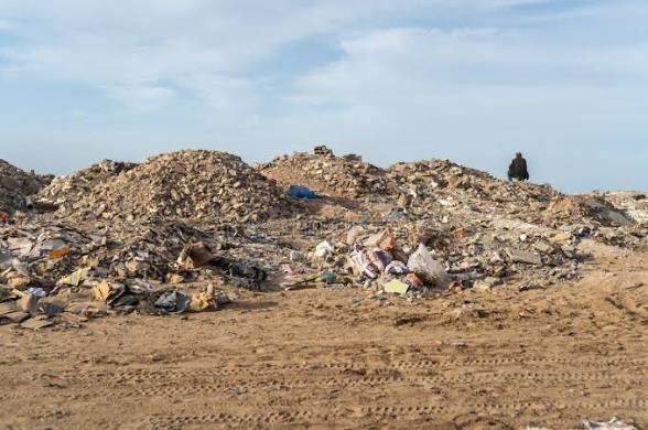 A lone figure stands atop massive piles of rubble, debris, and trash stretching across a barren dirt landscape under a hazy sky. The overwhelming sea of waste fittingly illustrates the post's joke about the Dallas Cowboys defense—a defense so porous and ineffective that it's compared to being lost in a dump.