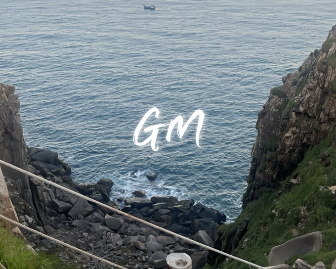 A view of a rocky coastline with the ocean stretching to the horizon, featuring a small boat and the handwritten text 'GM' overlaid on the image.