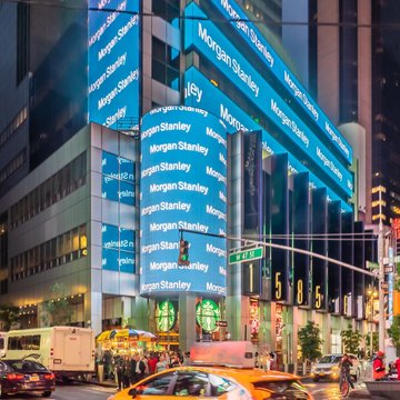 A nighttime view of a Morgan Stanley building, illuminated in vibrant blue with the firm's name repeated across its facade, alongside the iconic "1855" entrance marker—visually reinforcing the news that the financial giant has launched a Digital Asset Lab to explore stablecoins, tokenization, and DeFi applications.