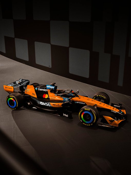 The image displays a McLaren Formula 1 race car in a dynamic pose against a checkered backdrop, featuring prominent sponsors like OKX, Velo, Gemini, and DP World. Despite the post suggesting "The style is not...," the sleek, glossy rendering with bold colors and dramatic lighting embodies a polished, professional automotive photography aesthetic rather than an unconventional or non-style approach.
