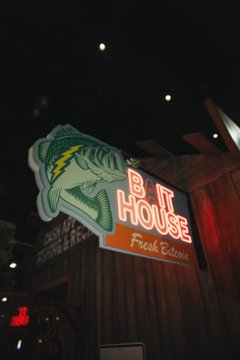 A neon sign for "Big House" featuring a fish illustration and the words "Fresh Catchun" glows brightly against the night sky. The caption "they're ni₿₿lin n' ₿itin" connects to the "Big House" branding, playing on the idea of getting "nibblin' and bitin'" at a seafood spot.