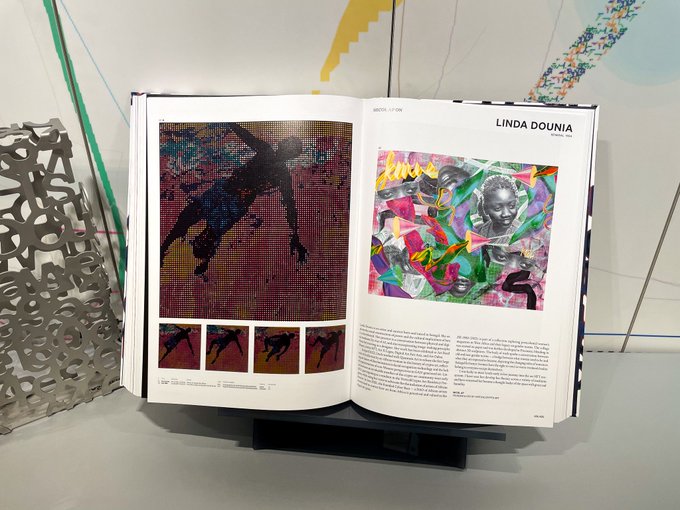 An open art book displays colorful mixed-media artwork by LINDA DOUNIA on the right page, with the left page showing a pixelated figure artwork by a different artist.
