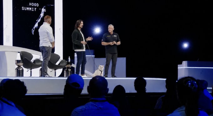 A presentation on stage at 'HOOD SUMMIT '26' with three people speaking to the crowd, including a Husky dog sitting on stage.
