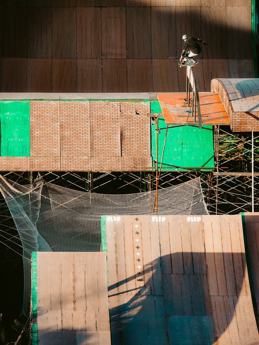 A top-down view of a stunt performer on a motorcycle ramp above a safety net at an extreme sports venue.