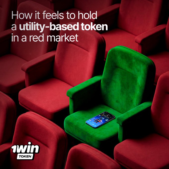 The image shows a green chair with a cell phone placed on top of it. The chair appears to be located inside an auditorium or theater, as there are multiple chairs visible in the scene. The text above the chair reads "How it feels to hold a utility-based token in a red market". This phrase is likely a reference to the concept of utility tokens and their potential value within a red market.