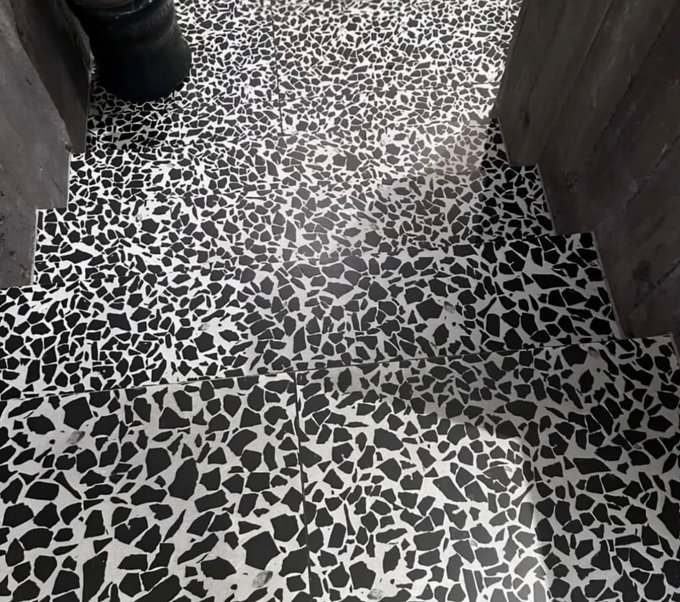 A wet terrazzo-style tiled floor in black and white, located between wooden walls.