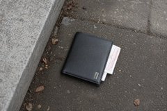 The image shows a black wallet laying on its side on the ground, with some papers inside of it. The wallet appears to be empty or has been misplaced by someone. The surrounding area seems to be an outdoor setting, possibly near a sidewalk or street. There is also a small amount of text in the image that reads "Google 身份验证器". This suggests that the wallet might have been lost or misplaced and could potentially contain sensitive information about the owner's identity or personal details.