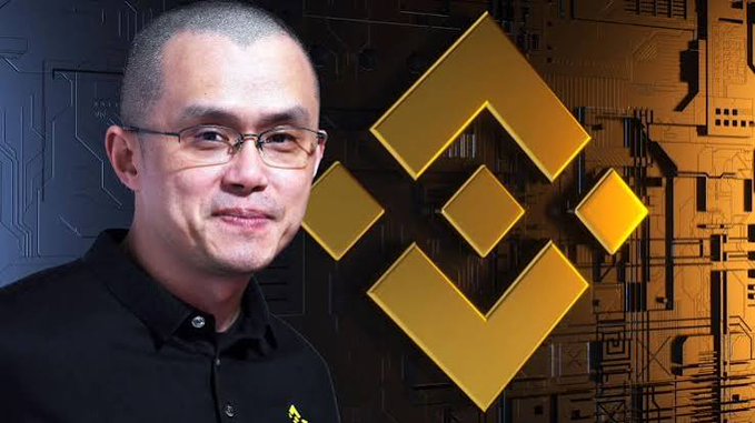 A portrait of a man with glasses in a black shirt standing next to the large golden Binance logo on a circuit board background.