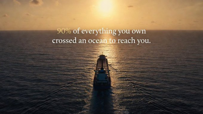 An aerial view of a cargo ship sailing on the ocean at sunset, overlaid with the text '90% of everything you own crossed an ocean to reach you.'