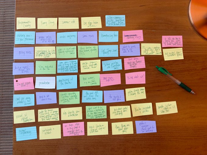 A collection of colorful sticky notes (pink, blue, yellow, purple) with handwritten text arranged on a wooden table, suggesting a brainstorming session.